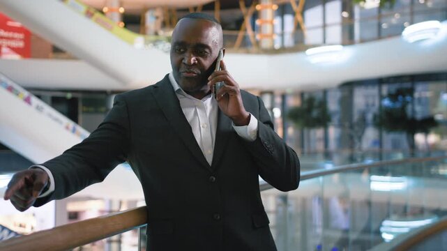 Happy cheerful 50s African American business man communicate with mobile phone call smiling in shopping mall ethnic mature businessman male professional talking with smartphone smile indoor in company