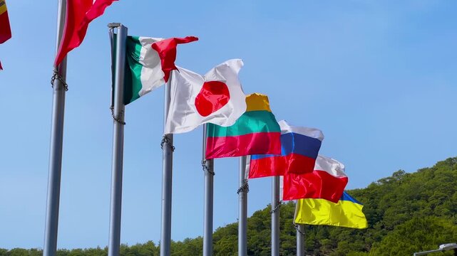 Row of national flags of Switzerland, Italy, Japan, Lithuania, Russia Poland and Ukraine on tall metal poles against clear blue sky. International relations, cooperation and diplomacy concept