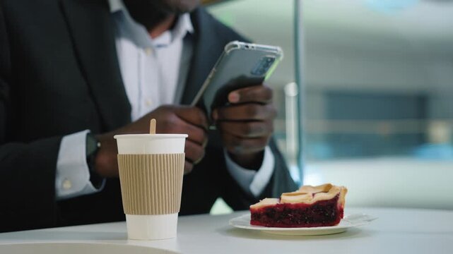 Cropped view male hands of unrecognizable business man holding mobile phone in cafe at table with coffee tea and berry cake pie African American businessman employer agent with smartphone network chat