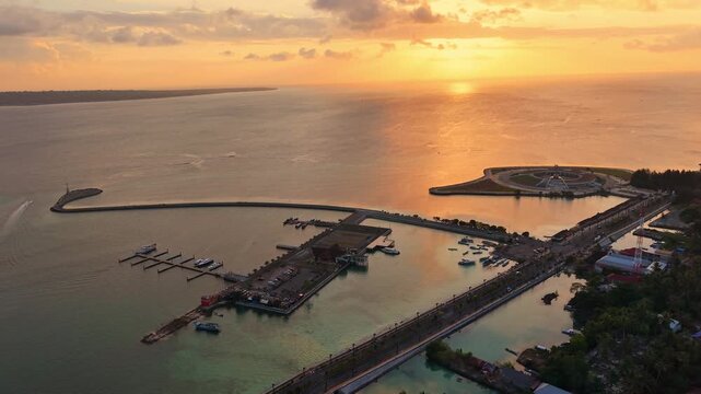 Aerial view of Marina Togo Wakatobi at sunset with boats docked at the pier and golden light reflecting on the sea in Kabupaten Wakatobi, Sulawesi Tenggara, Indonesia.