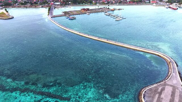 Aerial view of Marina Togo Wakatobi with its curved pier extending into the clear turquoise waters of the coral reef in Kabupaten Wakatobi, Sulawesi Tenggara, Indonesia.