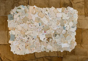 a large, overlapping collection of vintage handwritten letters, envelopes, postcards, and postal stamps arranged in a flat-lay collage on a burlap backdrop © Roberto Sorin