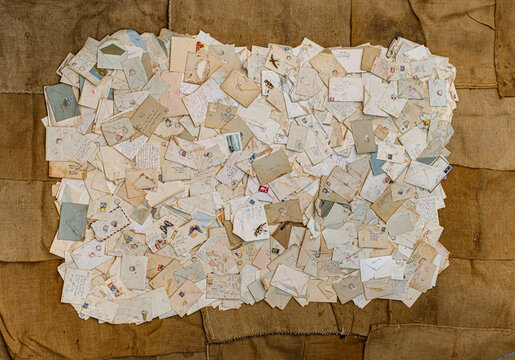 a large, overlapping collection of vintage handwritten letters, envelopes, postcards, and postal stamps arranged in a flat-lay collage on a burlap backdrop