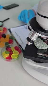Looking at candy samples under a microscope in a lab setting with colored sweets and notes