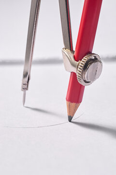 metal drawing compass sketching circle on white paper, drafting instrument with red pencil in macro close-up view, architectural engineering and geometry education concept