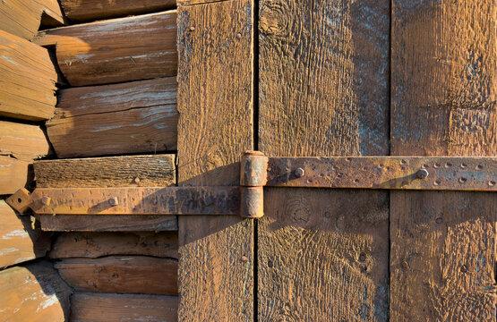 Close-up view of a rusted antique hinge on a log wooden building
