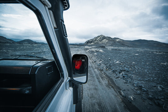 View from an offroad vehicle driving through the remote Icelandic Highlands, with a rugged gravel road, volcanic terrain and dramatic mountains under a cloudy northern sky in the wilderness.