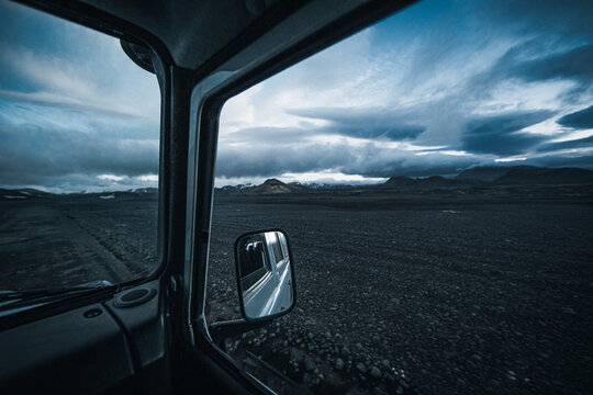 View from an offroad vehicle driving through the remote Icelandic Highlands, with a rugged gravel road, volcanic terrain and dramatic mountains under a cloudy northern sky in the wilderness.