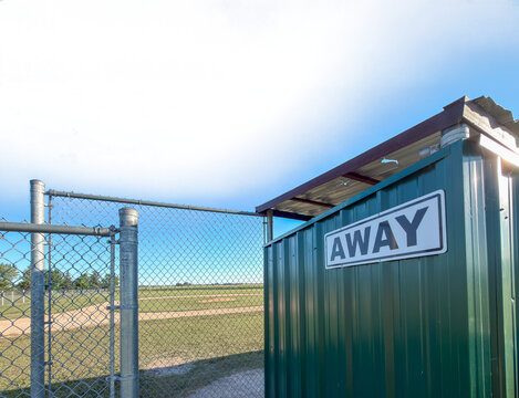 Home bench for a Away Team little league team next to a baseball diamond with a transparent sky

