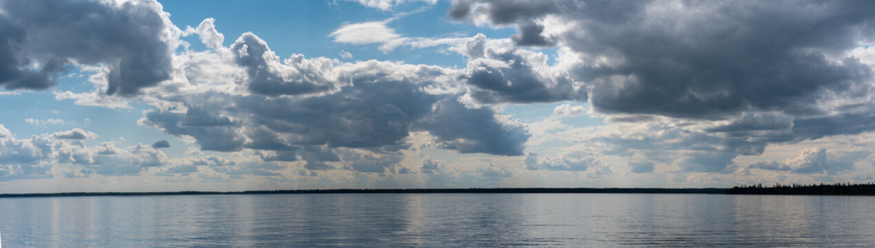 Panorama of large calm lake with a blue summer sky puffy clouds
