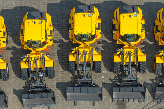 Aerial view of yellow wheel loaders parked in a row on a paved construction site in Poland.
