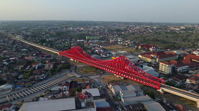 Aerial view of the red Joglo Railway Bridge spanning over the urban landscape of Kecamatan Banjarsari, Jawa Tengah, Indonesia.