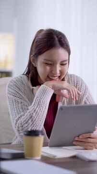 Young Asian student using tablet for online learning with headphones and coffee in modern study space