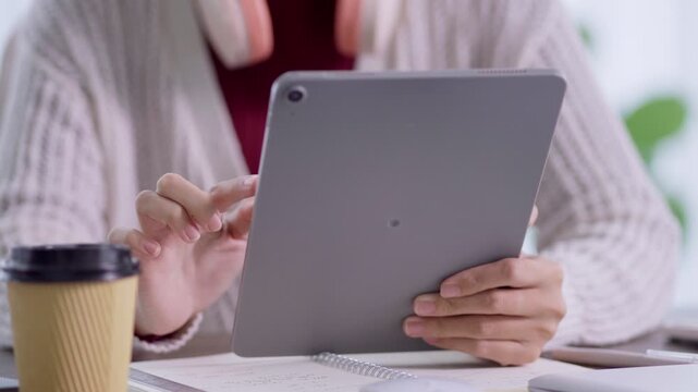 Asian student using digital tablet for online education with coffee and notebook at desk