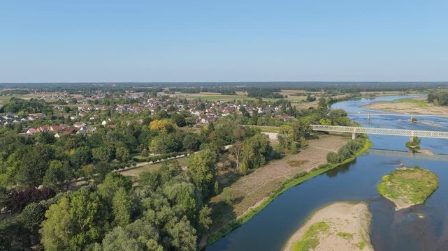 The picturesque town of Sully-sur-Loire in France, featuring the Loire River, a bridge crossing the water, lush green trees, and the surrounding countryside under clear blue skies, aerial view.