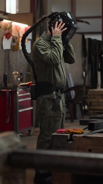 Vertical video of young adult Caucasian male welder putting on protective helmet with air respirator and pulling on heavy gloves in workshop. Footage is perfect for industrial safety campaigns
