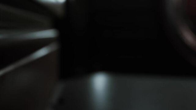 A person sits at a table in a low light setting. The surroundings are dark, and only a small light is visible. Sounds of chatter can be heard in the background.