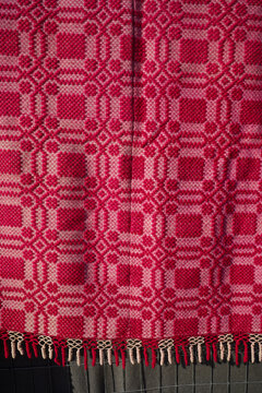 Close-up texture of a traditional Greek handwoven woolen textile in vibrant red and white. Intricate geometric folk art pattern featured with a red fringed border.