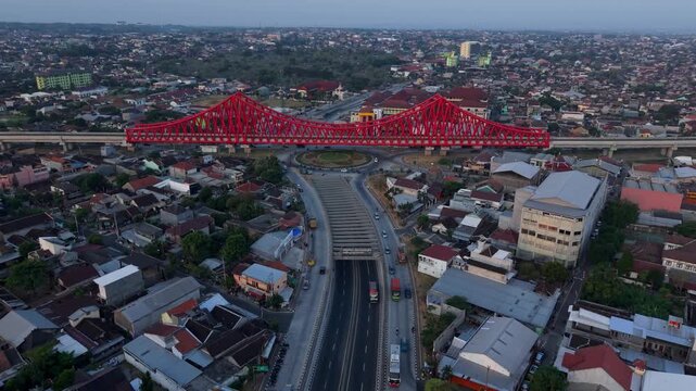 Aerial view of the iconic red Joglo Railway Bridge spanning over the urban road and underpass in Kecamatan Banjarsari, Jawa Tengah, Indonesia.