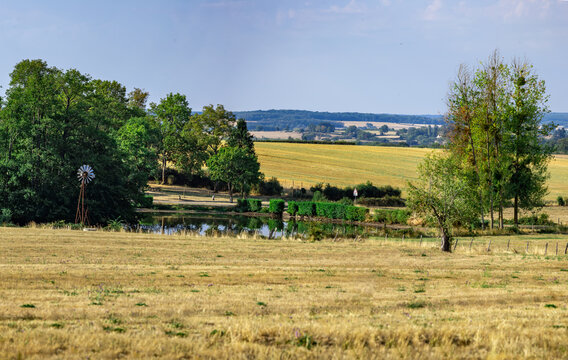Rural countryside landscape with mowed wheat field tractor plowing and water windmill
