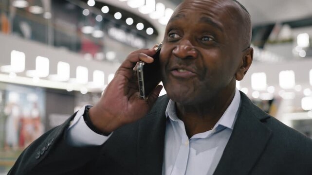 Happy African American business man talking mobile phone smiling walking in company. Mature ethnic businessman male entrepreneur professional manager talk smartphone call smile walk in shopping mall