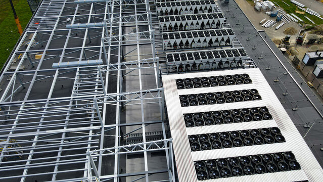 Data center rooftop under construction featuring structural framing alongside operational cooling units and numerous fans, illustrating the ongoing development of critical infrastructure