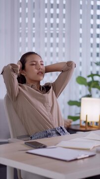 Young Asian student experiencing stress and headache while studying at home desk with paperwork