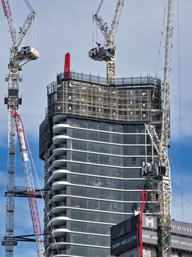Aerial view of a modern skyscraper under construction featuring a glass facade, white balconies, and multiple tower cranes in Surfers Paradise, Queensland, Australia.