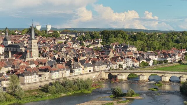 La Charite-sur-Loire, France, featuring the town's picturesque rooftops, the prominent church with its tall spire, and the historic stone bridge crossing the Loire River, aerial view.