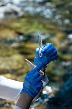 industrial wastewater testing river landscape with copy space for banner design, person in blue gloves holding glass tube with water sample, testing for heavy metal poisoning and chemical pollution