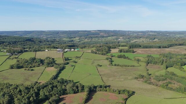 The rural landscape in Morvan, France, showing patchwork fields, green pastures, scattered farmhouses, and wooded areas under a clear blue sky, aerial view.