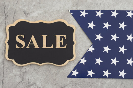 Sale text on a black chalkboard sign on marble with blue star banner pennant for patriotic sales