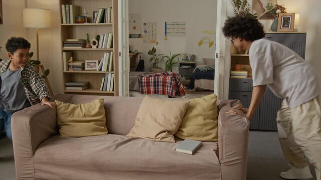 African American teenager and child playing tag, running around sofa and jumping on bed at home. Perfect for family lifestyle commercials or parenting campaign videos