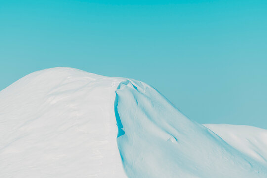 Smooth snow-covered hills under a clear blue winter sky, minimal landscape with soft curves, calm atmosphere, and clean natural background. Selective focus.