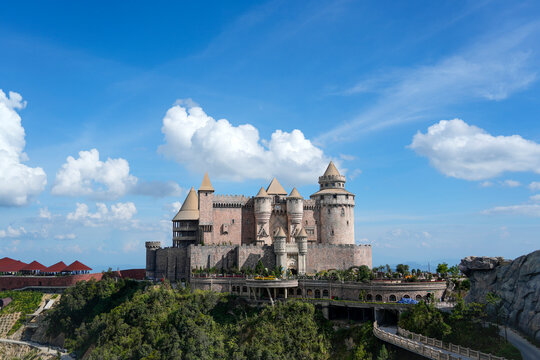 A stunning castle rises majestically on a green hill under a bright blue sky, enveloped by soft white clouds, inviting imagination and adventure