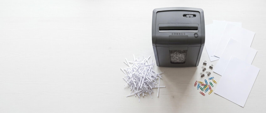 Office shredder with shredded papers and blank documents on desk  