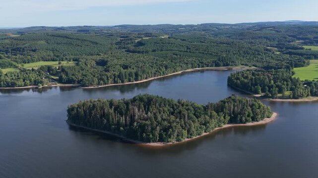 A densely forested island surrounded by the calm waters of Lac des Settons in the Morvan region of France, aerial view.