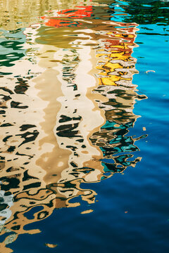 Impressionistic background of wave ripples reflecting urban architecture along a river bank. Concept of waterfront living, urban reflection, artistic texture, and summer light.