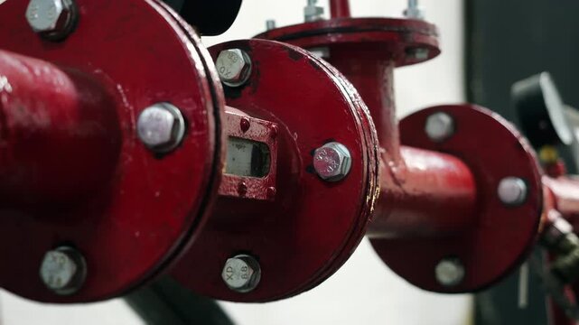 Close-up of red metal pipes with bolted flange connections in a fire suppression system. Industrial fire protection infrastructure and pipeline equipment.