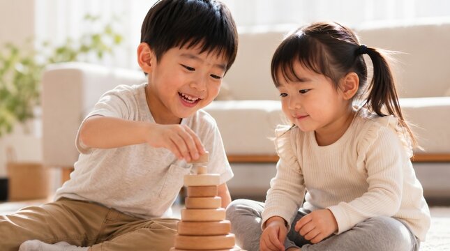 Cute Asian little boy and girl playing together with wooden ring stacker toy on the floor, happy siblings in a bright modern home, early child development concept