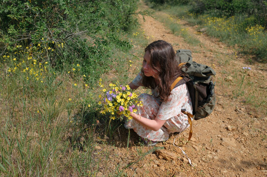 Woman with backpack picking wildflowers along a country path