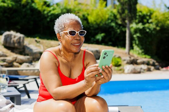 Senior woman enjoying poolside leisure using mobile phone