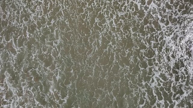 Aerial view of ocean waves crashing with white foam patterns on the dark sea surface in Maragogi, Alagoas, Brazil.