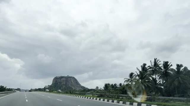 Full HD driving footage on a wet curving highway with cars and yellow truck passing through lush green roadside trees, cloudy sky and rural landscape, capturing monsoon road trip and travel journey.