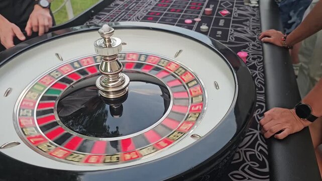 People gather around a roulette table to play at an outdoor event in the afternoon