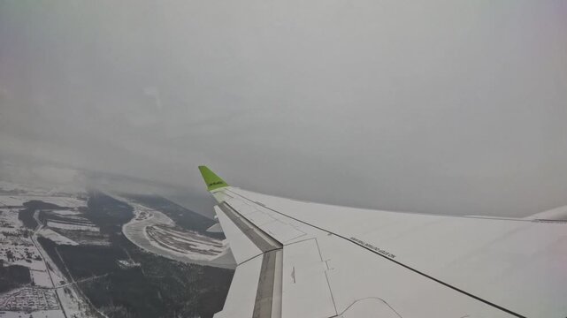 RIGA, LATVIA - FEBRUARY 10, 2024: AirBaltic airplane wing flying over frozen river and snowy coastline in winter