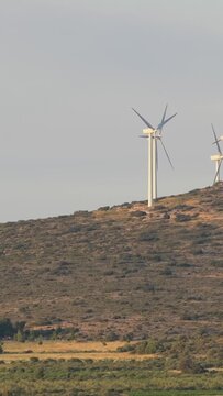 Wind turbines on a sunlit, shrub-covered hillside near Opoul Perillos, France, vertical 9:16 view.
