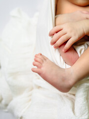 Obraz premium A charming close-up of a newborn's tiny foot stretching out beside delicate folded hands, wrapped in textured white blankets for a cozy studio shot.