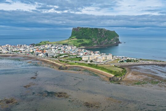 Aerial view of Seongsan Ilchulbong volcanic tuff cone rising above the coastal town and surrounding ocean in South Korea.