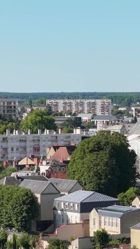 Nevers, France, showing a mix of modern apartment blocks and traditional French houses surrounded by lush green trees under a clear blue sky, aerial vertical 9:16 view.